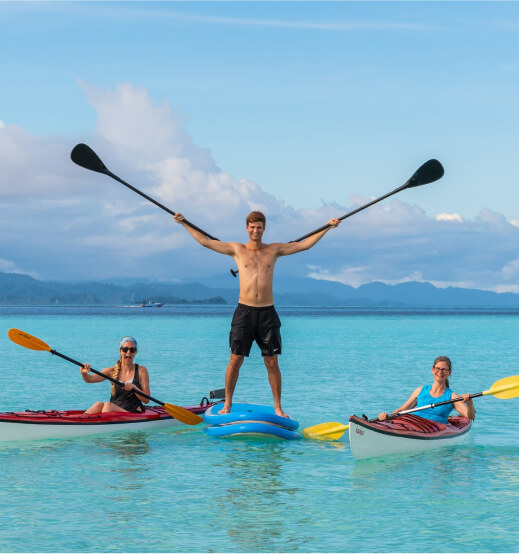 A man stands up on a paddle board and 2 women kayaking